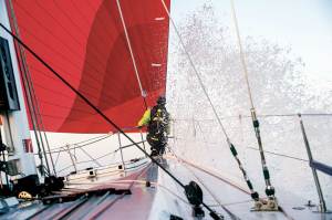 boat with red and white sails and a lot of spray from the ocean