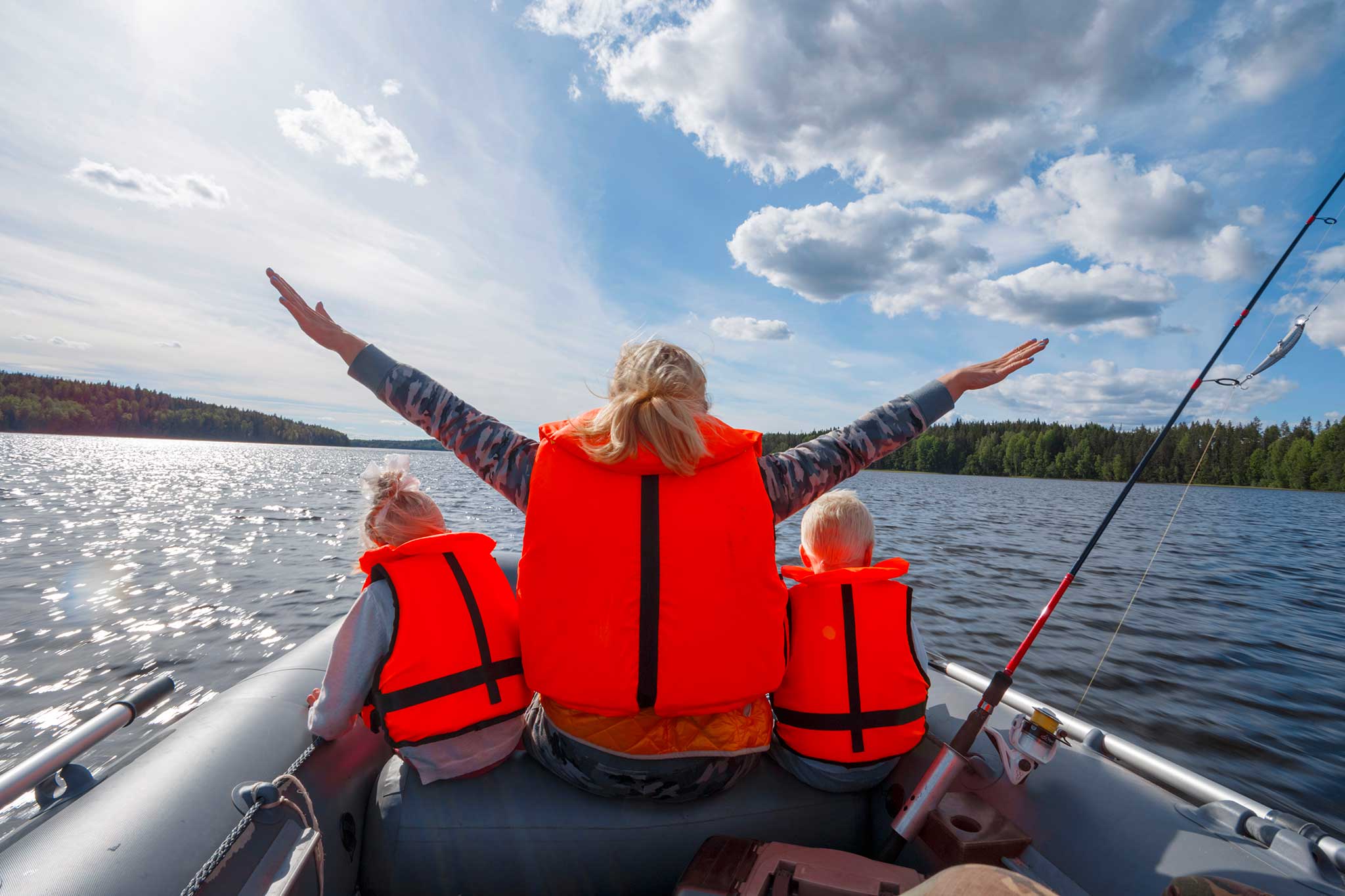 An adult and two children on a dinghy in the water wearing life jackets.
