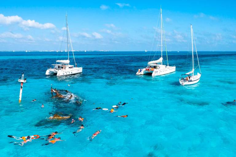 AdobeStock_444526170-bahamas-2607 Boats on the blue water and people swimming in the water.