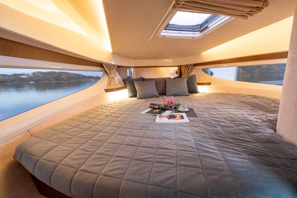 A large bed on a boat surrounded by windows