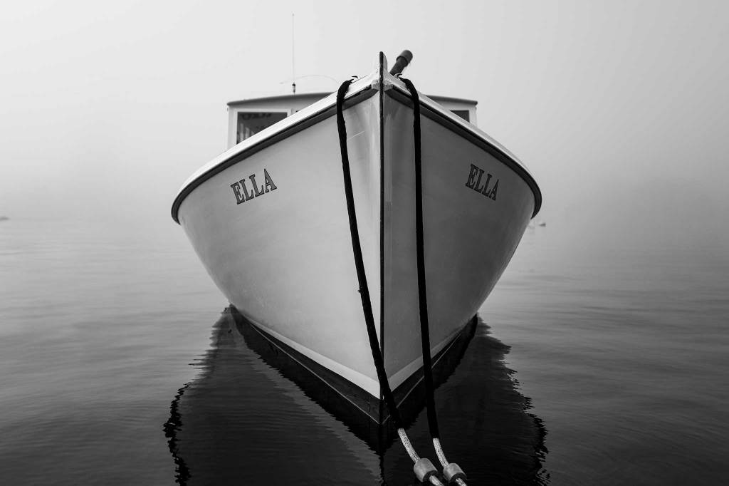 Black and white photograph of a small boat with its reflection on calm water