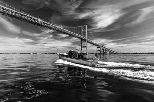 Onne-van-der-Wal-52131637-2 Black and white photograph of a boat motoring under a large bridge