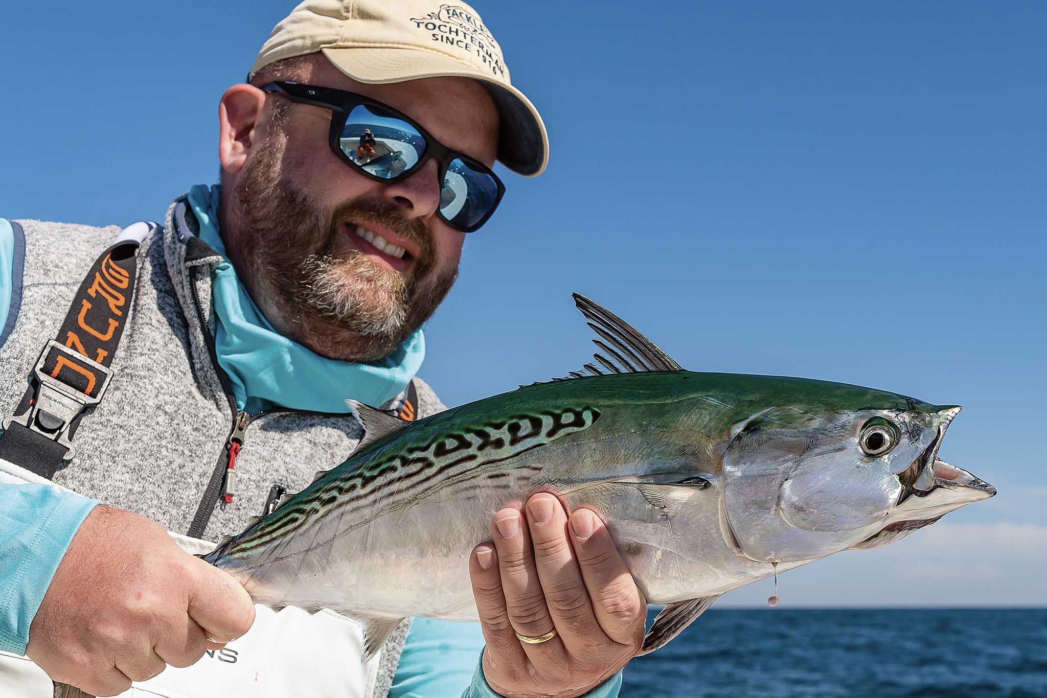 A man wearing a cap holding a fish out on the water