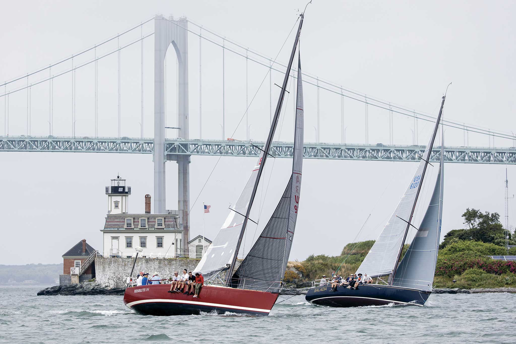 Two boats sailing with a bridge in the distance.