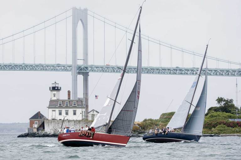 Two boats sailing with a bridge in the distance.