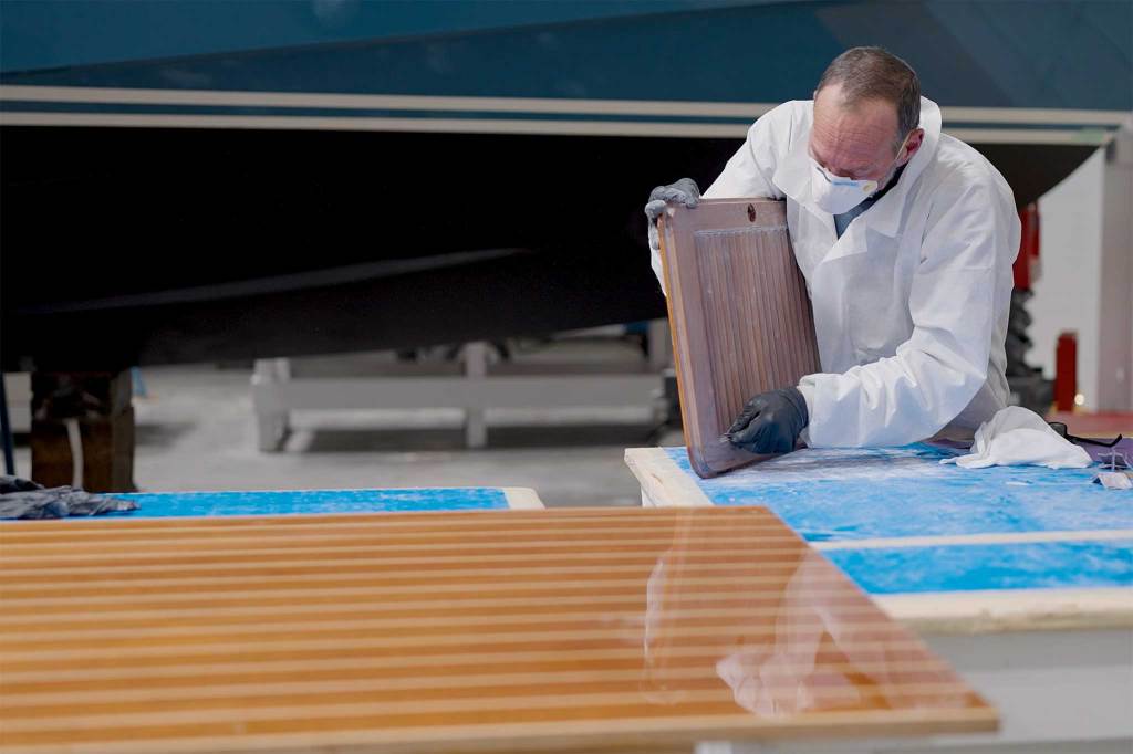 A man with a lab coat and mask studing a piece of wood in his hands and another slab of treated wood lying on the table in front of him